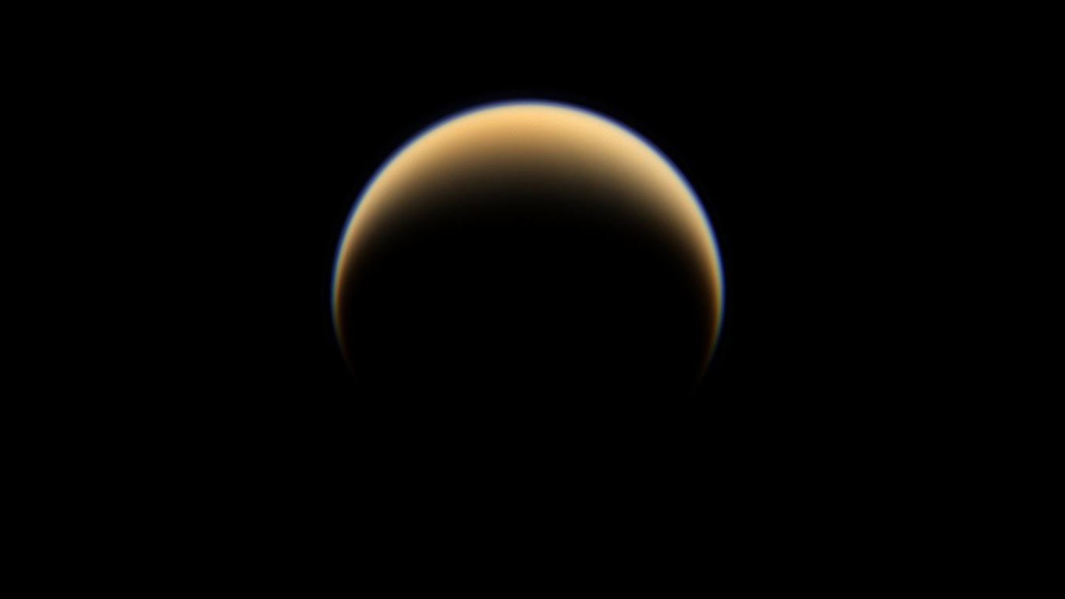 Titans beleuchtete gelb-orange Dunsthülle mit einem bläulichen äußeren Saum vor schwarzem Weltraum, Cassini-Aufnahme
